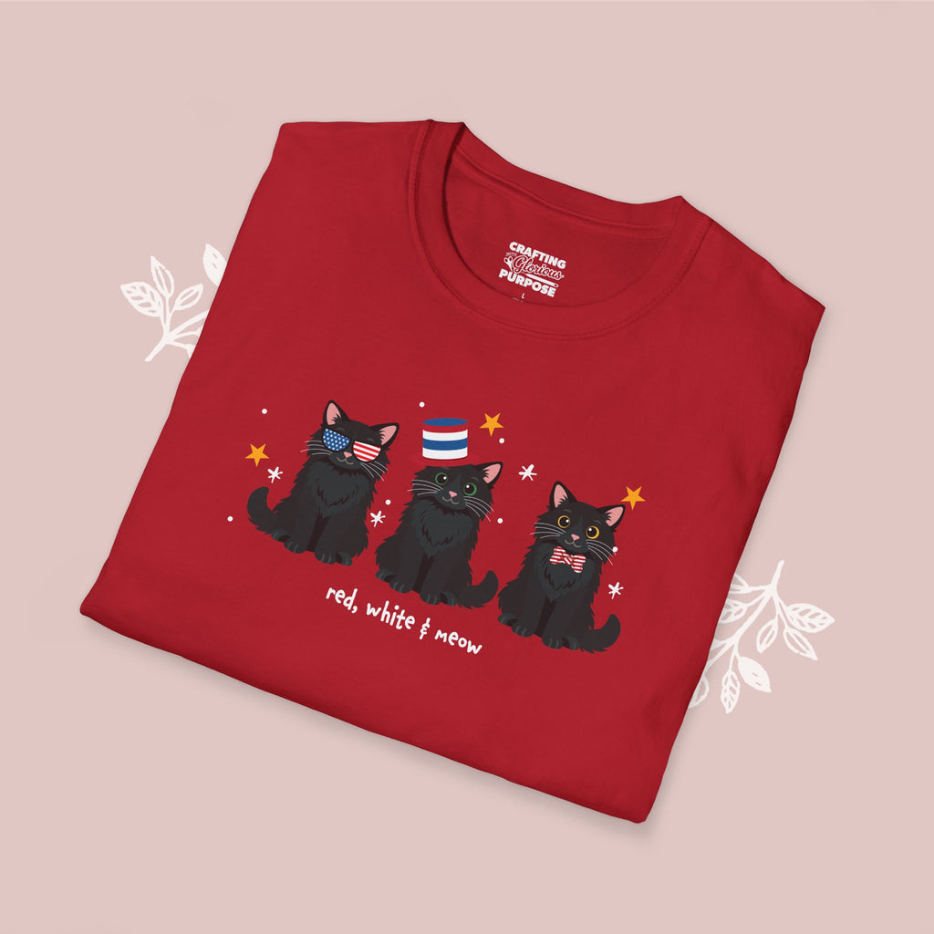 Folded red t-shirt with black cat illustration and text on a pink background