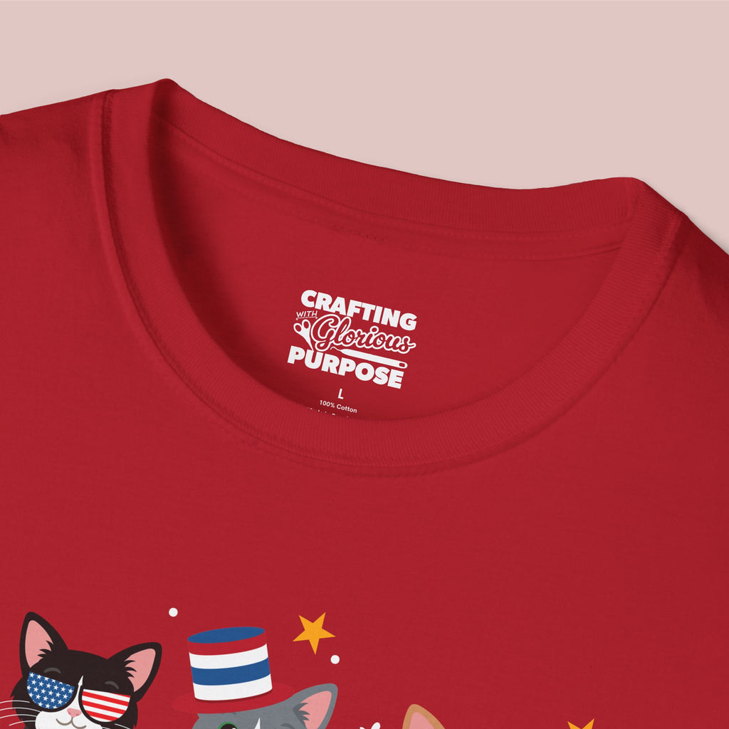 Red t-shirt with a graphic of cats wearing American flags and text 'Crafting a Glorious Purpose' on a pink background.