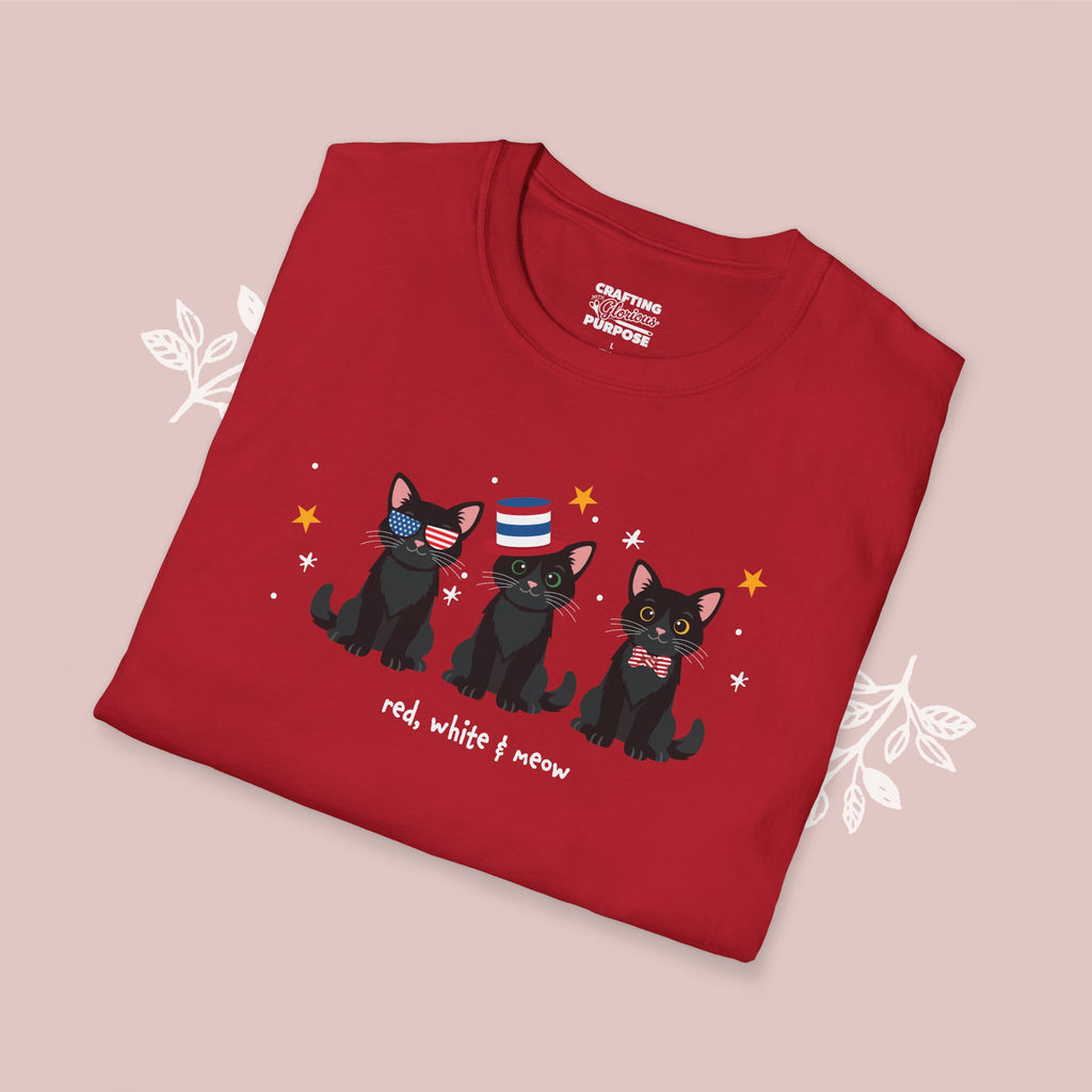 Folded red t-shirt with black cat illustrations and text on a pink background