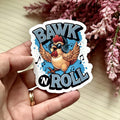 Sticker with a chicken and 'BAWK N ROLL' text held by a hand, with pink flowers in the background.
