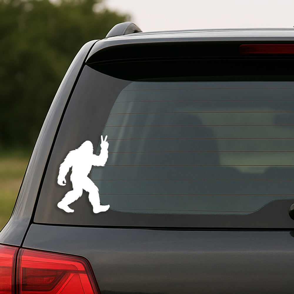White Bigfoot decal on a black car's rear window with a blurred natural background