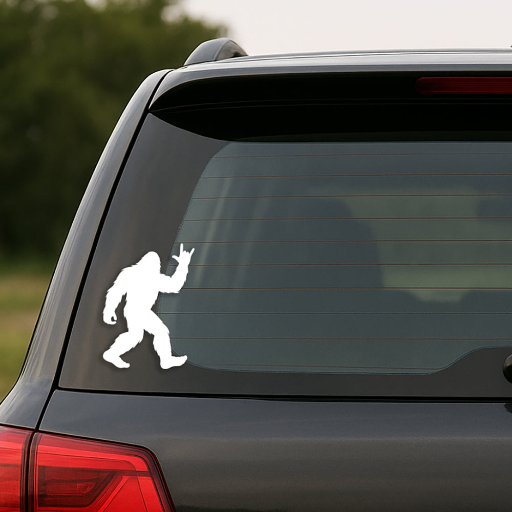 White Bigfoot decal on a black car's rear window with a blurred natural background