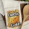 Kitchen towel with cheese-themed design and wooden spoon on a wooden surface
