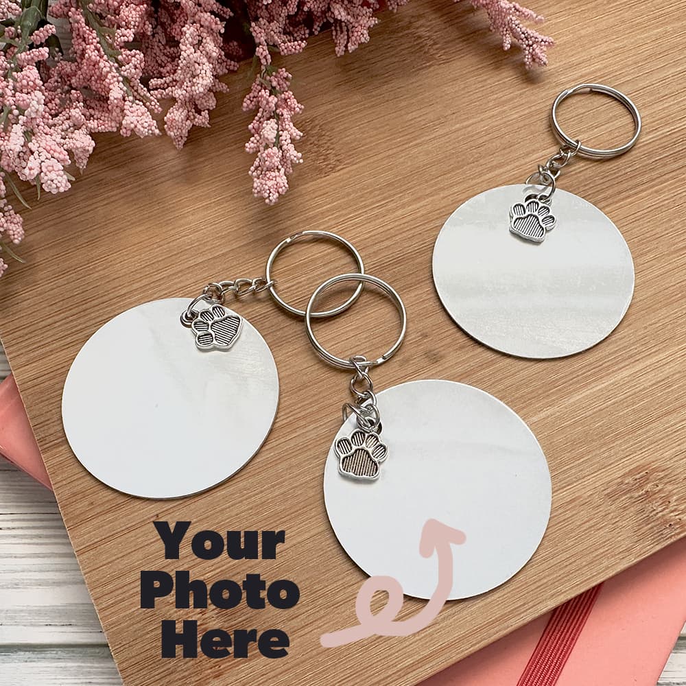 Three silver keychains with paw charms on a wooden surface with pink flowers.