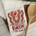 Kitchen towel with bacon design and text, wooden spoon on a wooden surface