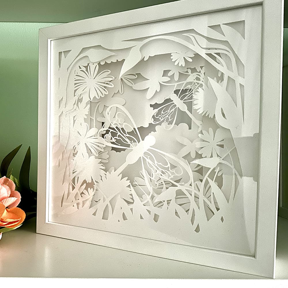 Decorative wall art with floral and dragonfly design in a white frame.