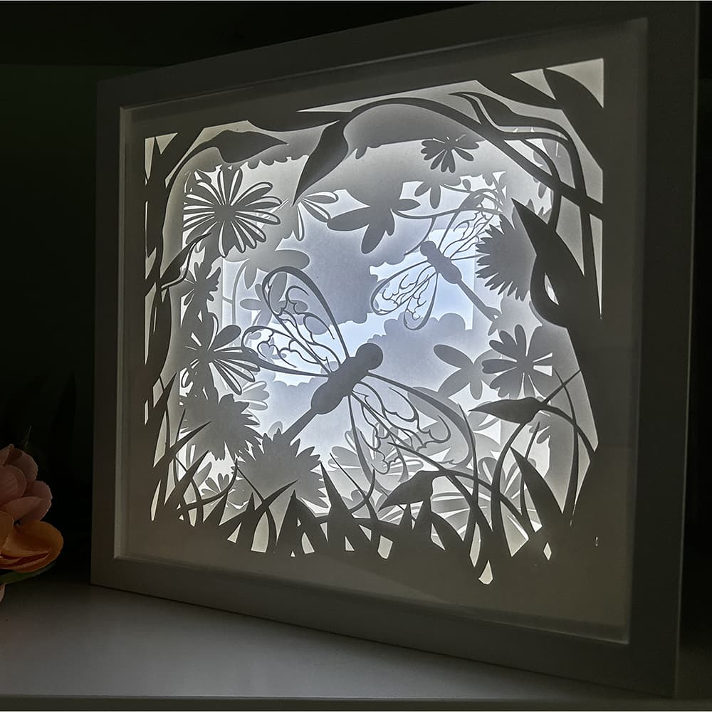 Framed paper cut art with dragonflies and floral design on a dark background