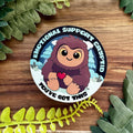Sticker with cartoon character holding a heart, surrounded by green leaves on a wooden surface