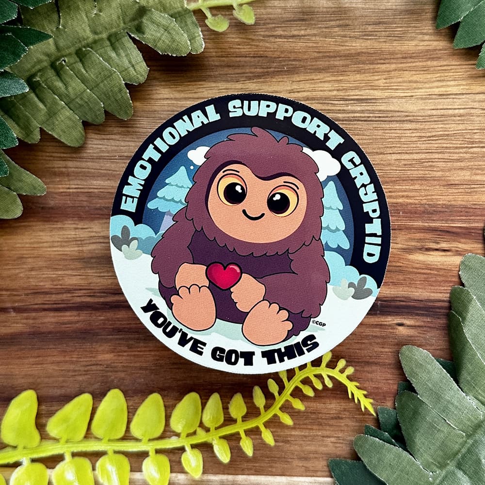Sticker with cartoon character holding a heart, surrounded by green leaves on a wooden surface