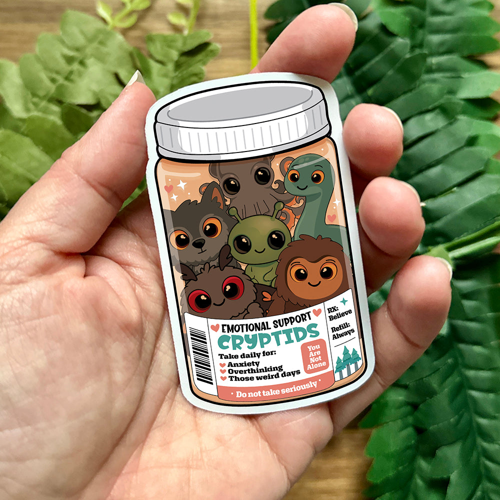 Hand holding a small jar with cartoon characters and humorous label against a green leafy background
