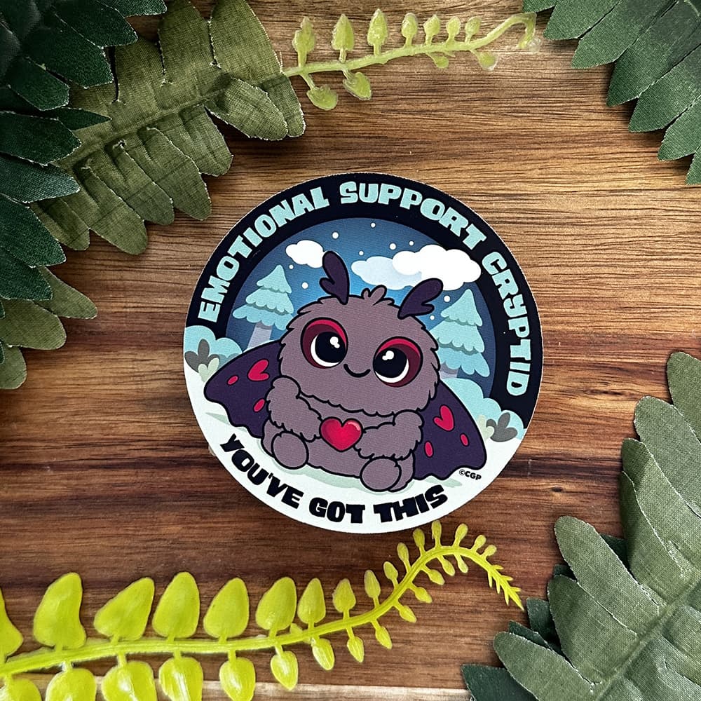 Cute sticker of Mothman on dark wooden board with greenery.