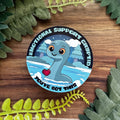 Emotional Support Cryptid sticker with heart and text on a wooden background with leaves