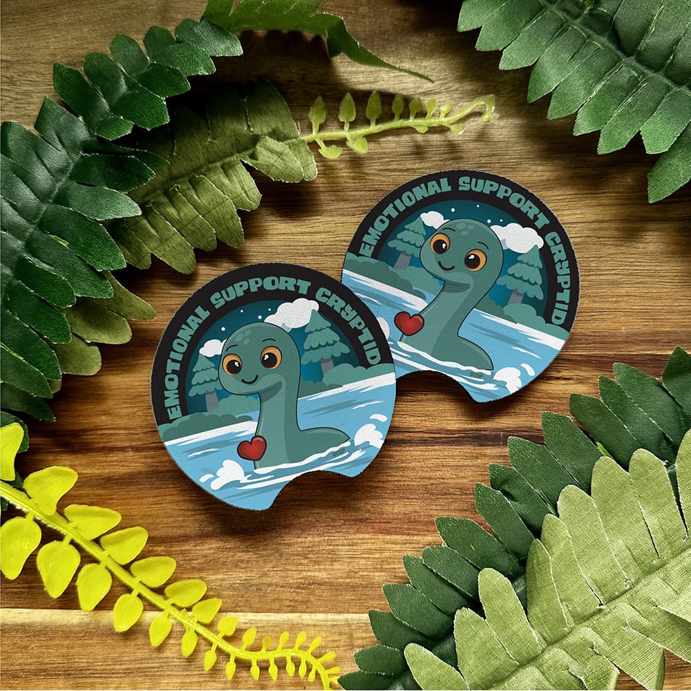 Two 'Emotional Support Crocodile' stickers on a wooden surface with green leaves.