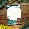 Notebook with cartoon Bigfoot design on a wooden surface with green leaves.
