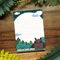 Notebook with a cute mothman design and text 'You've Got This' on a wooden surface with green leaves.
