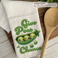 Kitchen towel with peas in a pod design and wooden spoon on a wooden surface