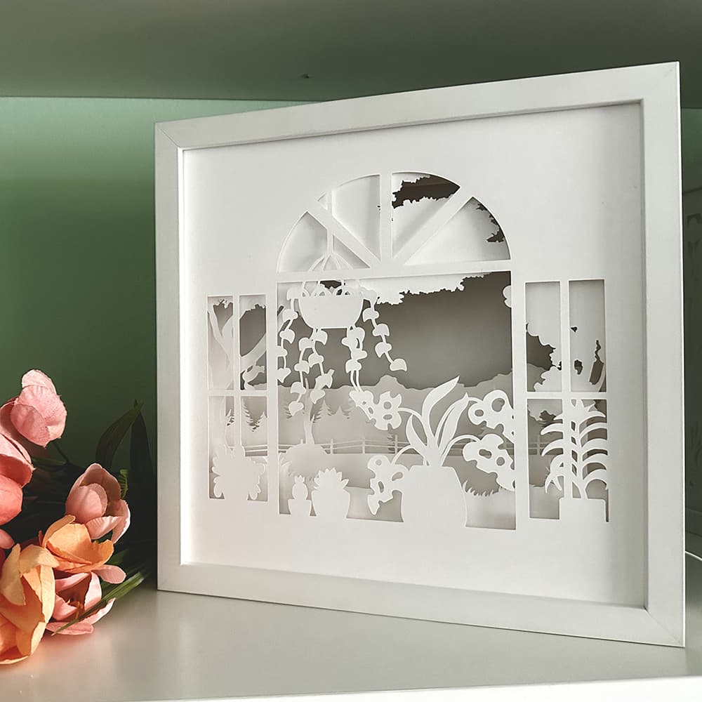 Framed paper cut art with garden scene on a green wall