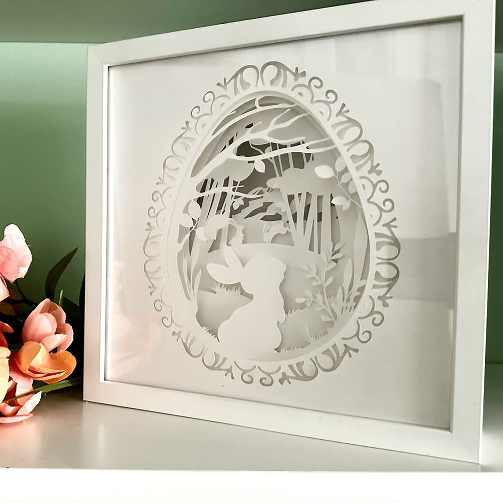 Framed paper cut art of a rabbit in a forest design on a light green background.