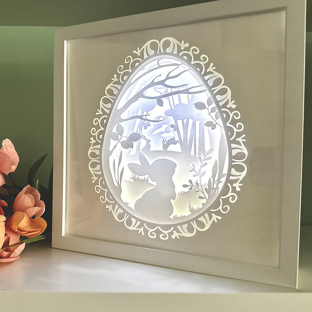Framed paper cut art of a rabbit in a forest scene with decorative border.