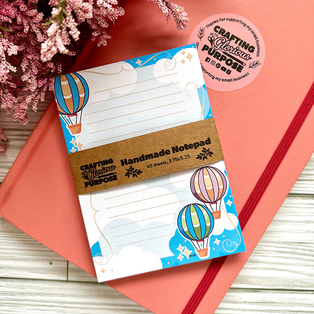 Handmade notepad with hot air balloon design on a pink surface with flowers.