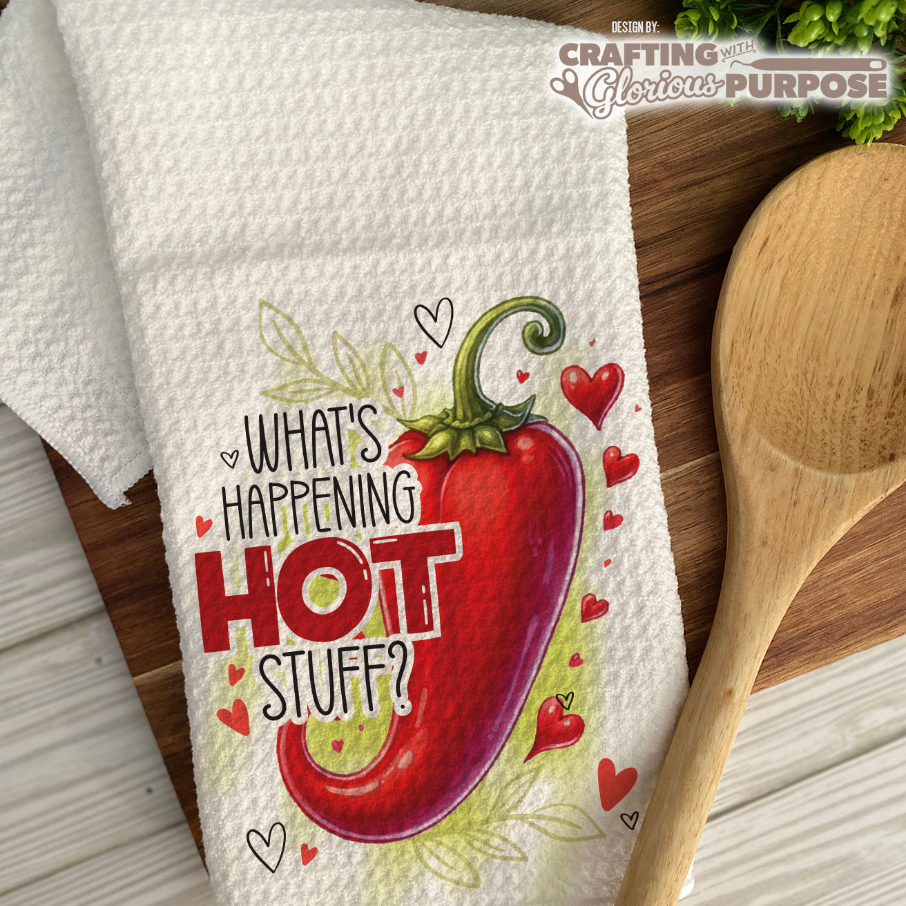 Dish towel with a red pepper graphic and text on a wooden surface with a wooden spoon.