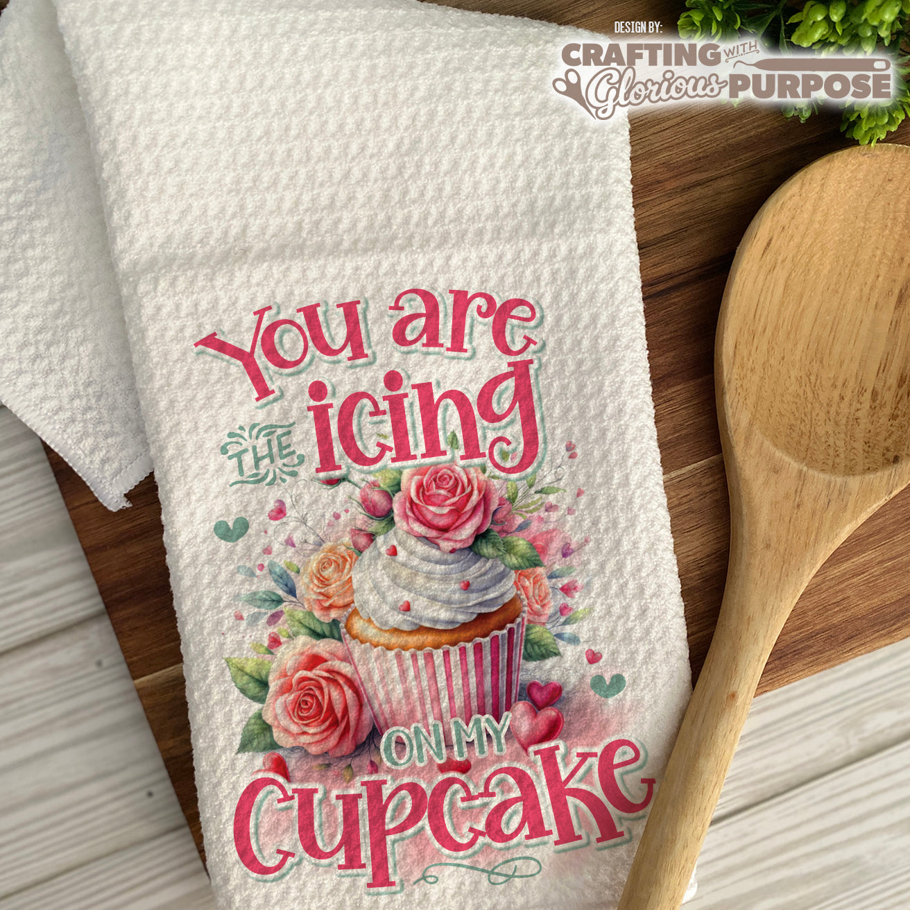 Decorative kitchen towel with a cupcake design and text on a wooden surface.