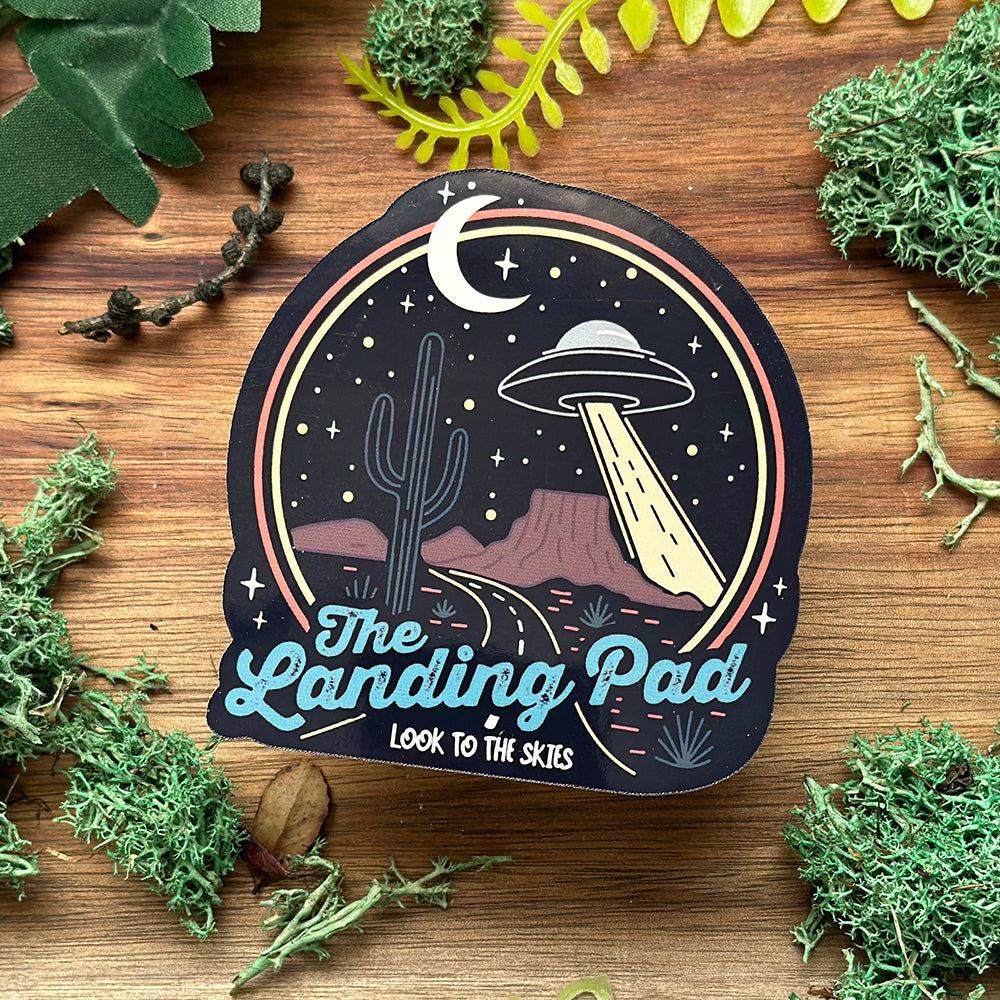 Sticker with UFO design on a wooden surface with greenery