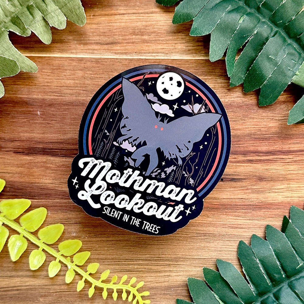 Sticker with Mothman design on a wooden surface with leaves