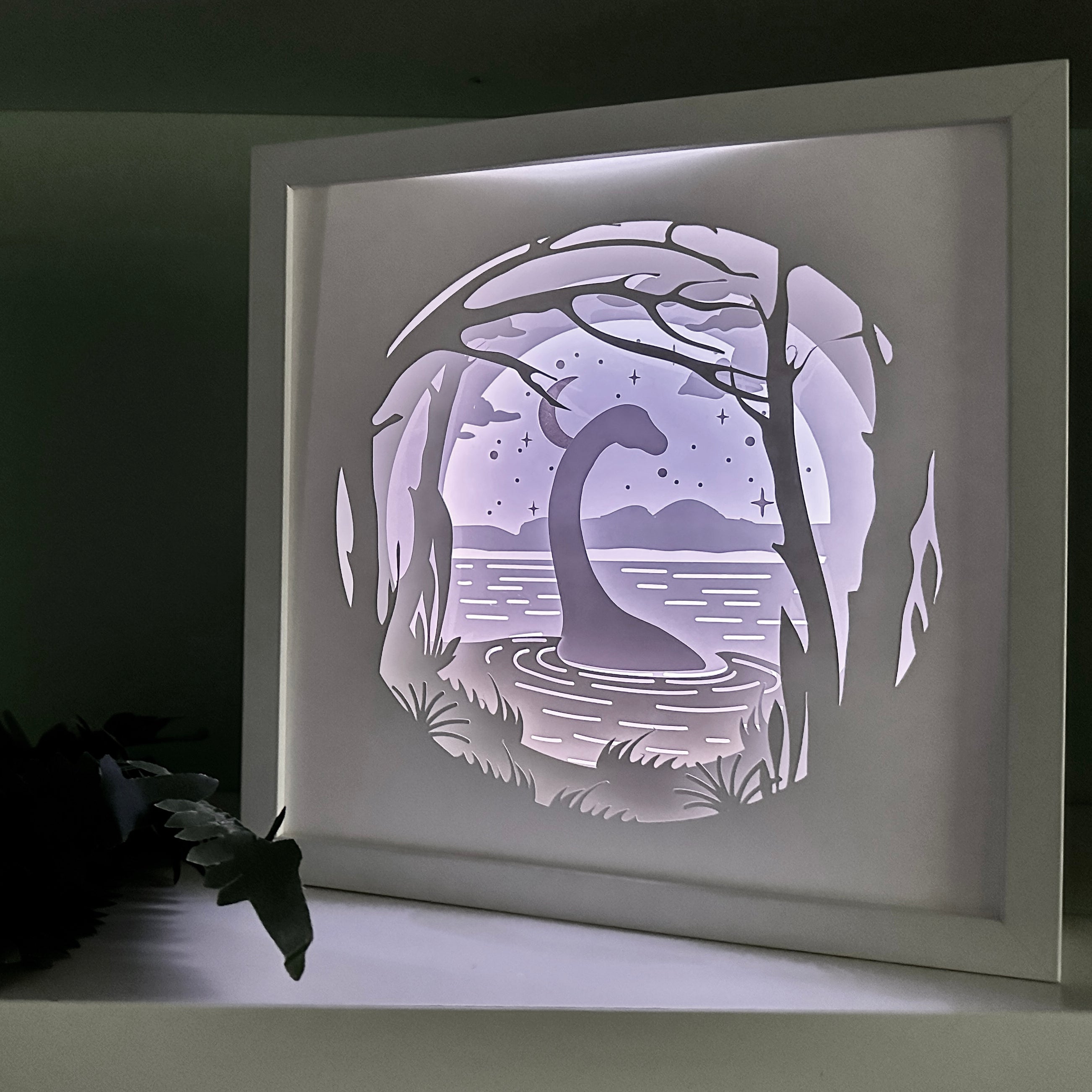 Framed paper cutout of a Loch Ness Monster design on a dark background