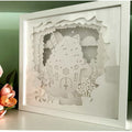 Framed paper cutout of a gingerbread house with decorative elements on a green background.