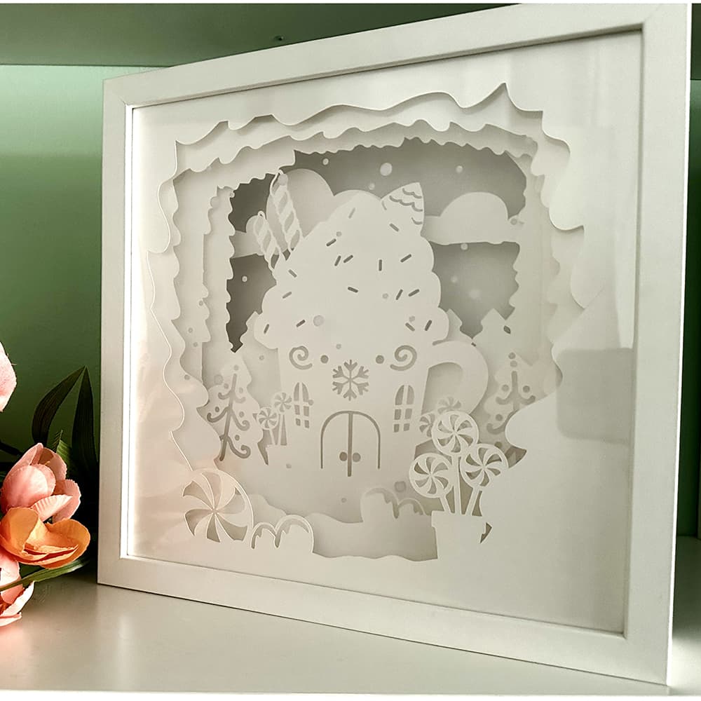 Framed paper cutout of a gingerbread house with decorative elements on a green background.