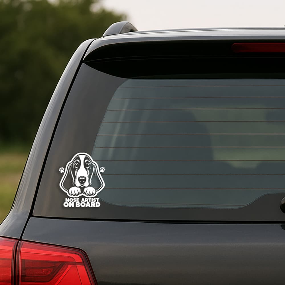 Car window with a sticker of a dog's face and 'Nose Artist on Board' text.