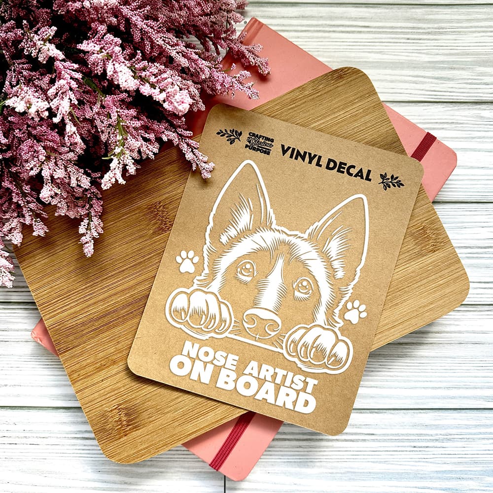Vinyl decal of a dog with 'Nose Artist on Board' text on wooden boards with pink flowers in the background.