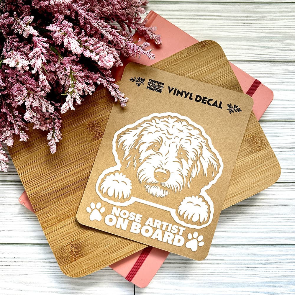 Vinyl decal with a dog illustration and text on a wooden board with pink flowers in the background.