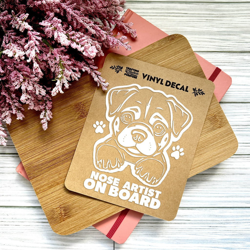 Vinyl decal with a dog illustration and text on wooden boards with pink flowers in the background.