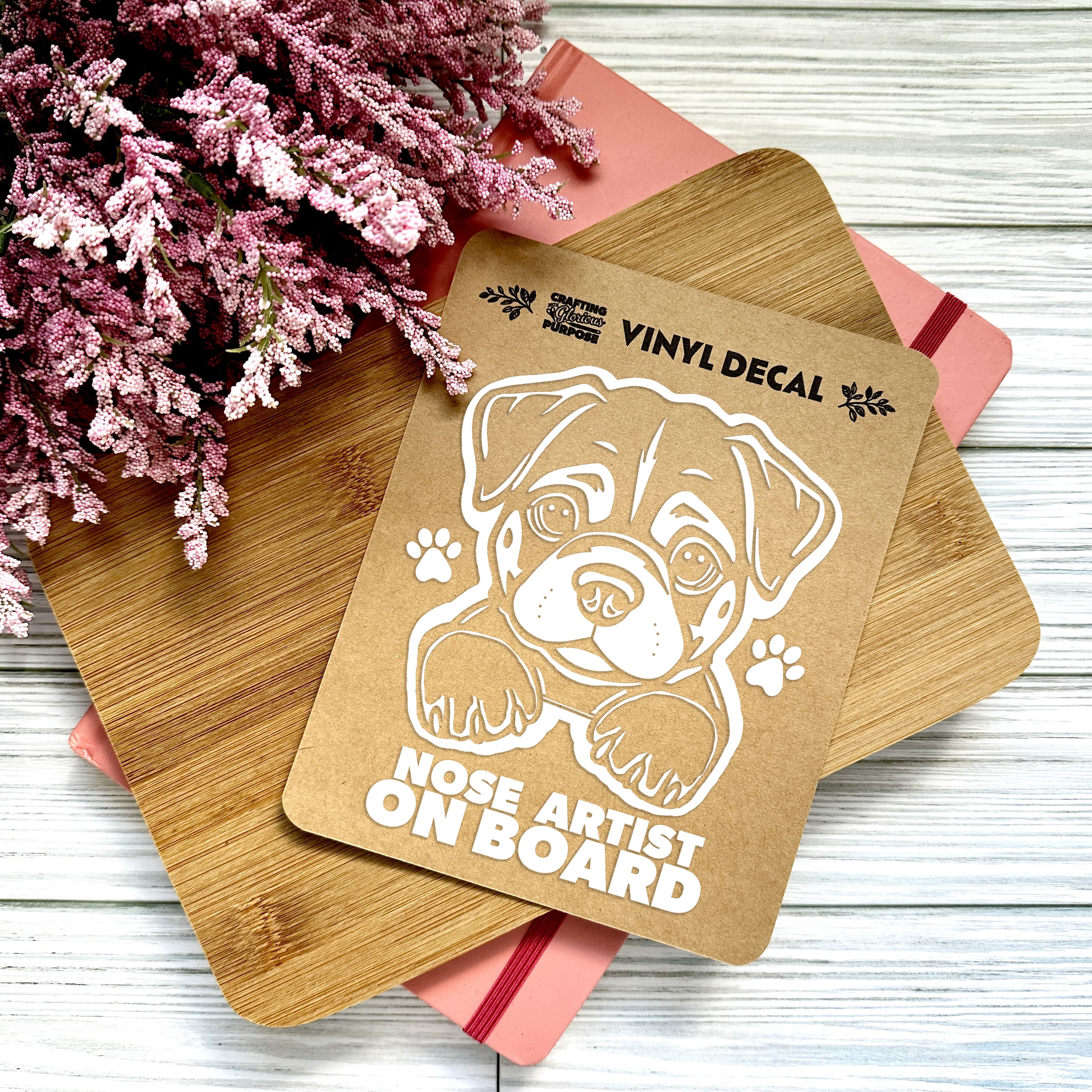 Vinyl decal with a dog illustration and text on wooden boards with pink flowers in the background.