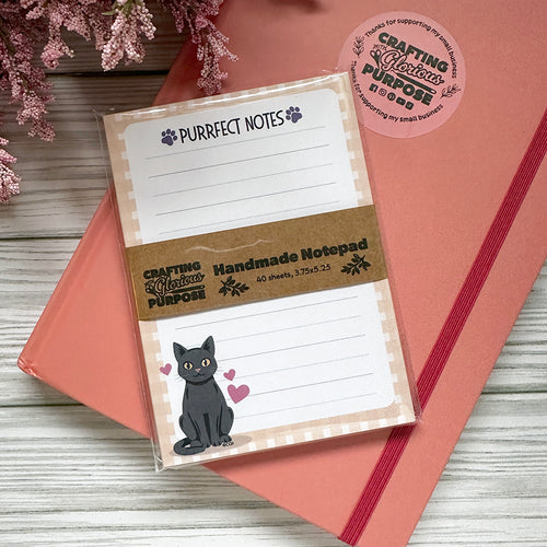 Notepad with 'Purrfect Notes' text and a cat illustration on a pink surface with flowers.