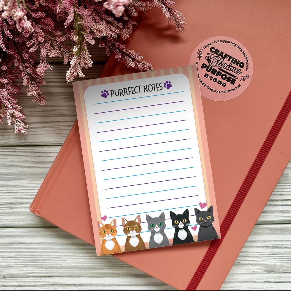 Notepad with 'Purrfect Notes' text and a cat illustration on a pink surface with flowers.