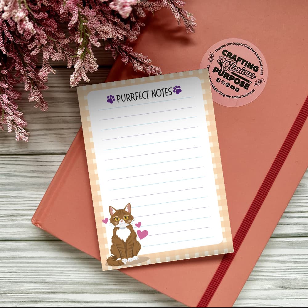 Notepad with 'Purrfect Notes' text and a cat illustration on a pink surface with flowers.