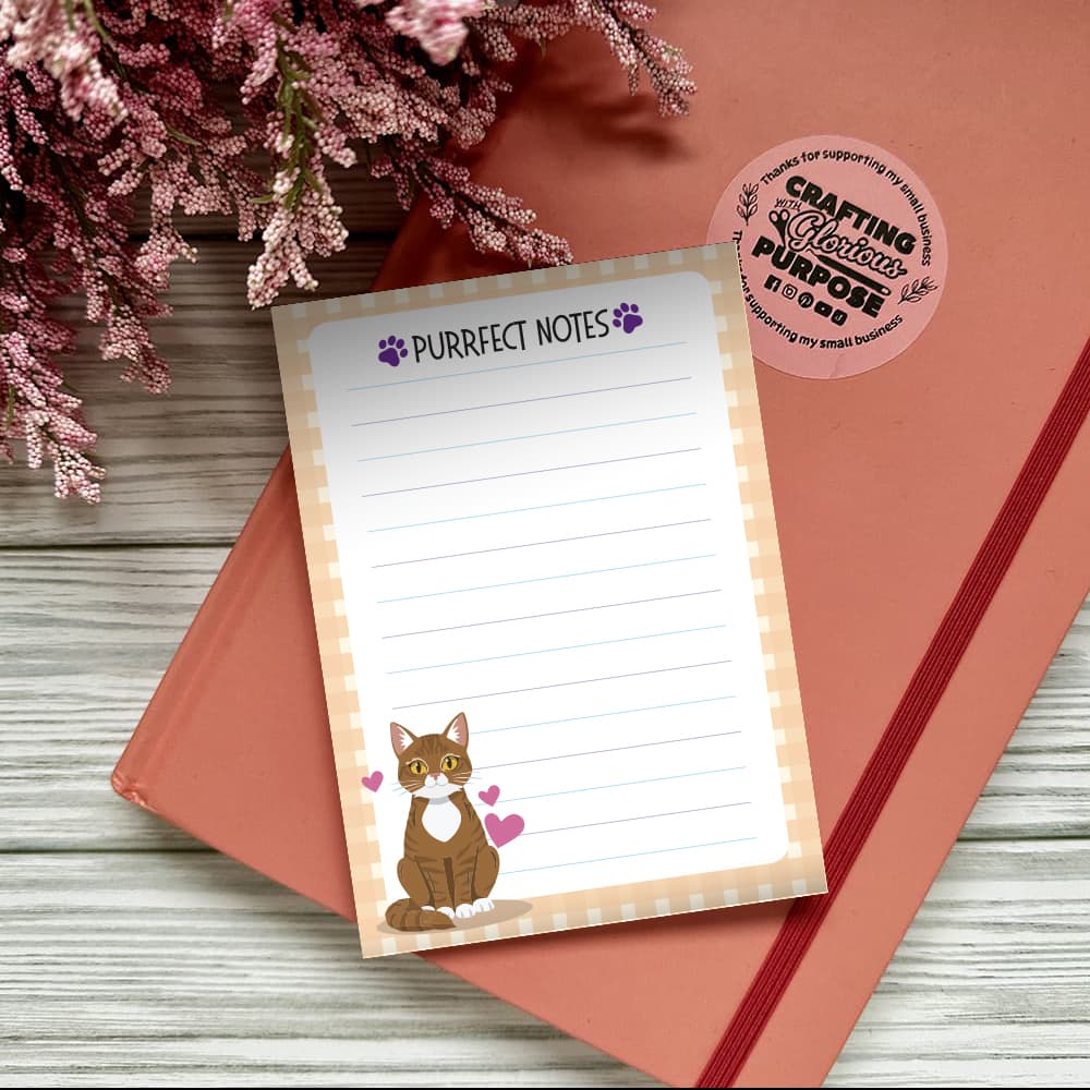 Notepad with 'Purrfect Notes' text and a cat illustration on a pink surface with flowers.