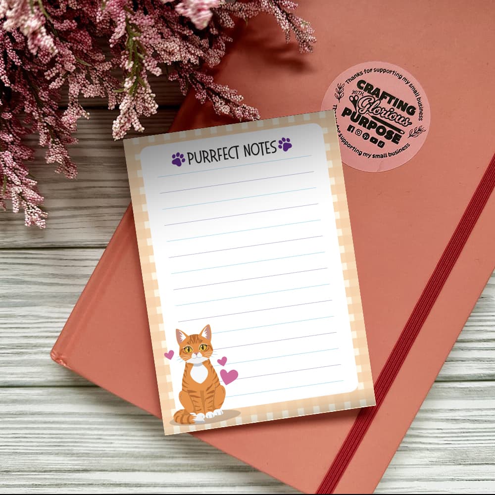 Notepad with 'Purrfect Notes' text and a cat illustration on a pink surface with flowers.