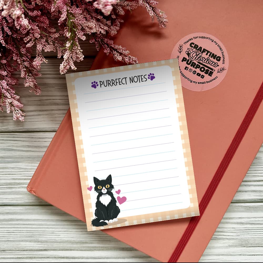Notepad with 'Purrfect Notes' text and a cat illustration on a pink surface with flowers.
