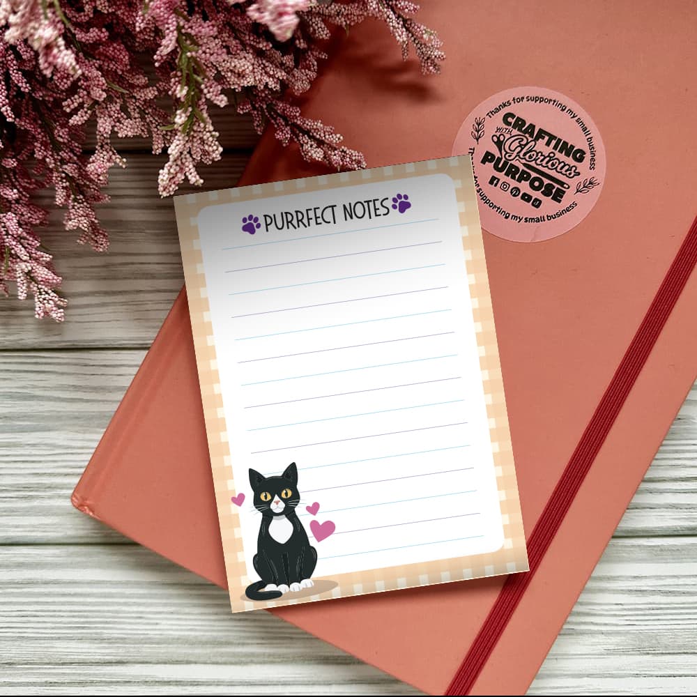 Notepad with 'Purrfect Notes' text and a cat illustration on a pink surface with flowers.