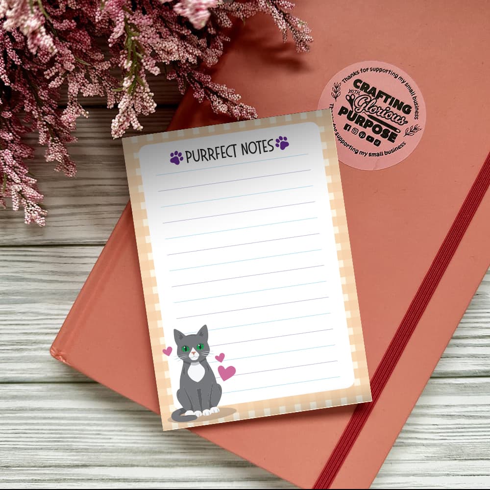 Notepad with 'Purrfect Notes' text and a cat illustration on a pink surface with flowers.