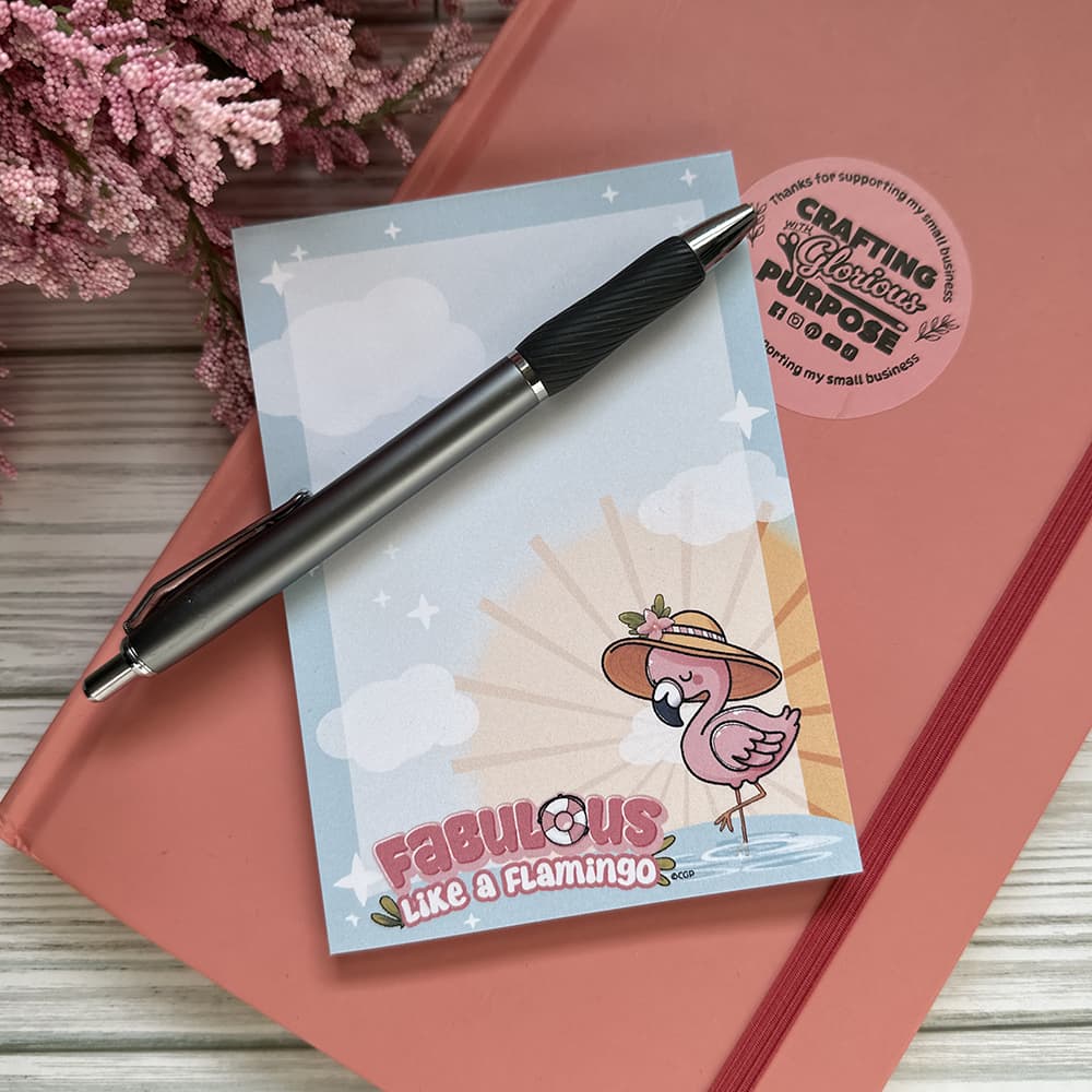Notebook with a flamingo design, pen, and decorative elements on a wooden surface.