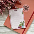 Notepad with plant designs on a wooden surface with pink flowers.