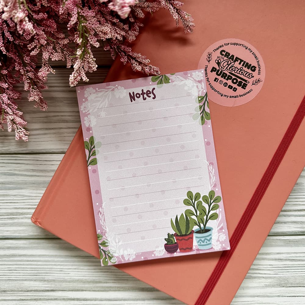 Notepad with plant designs on a wooden surface with pink flowers.