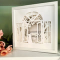 Framed paper art of a cat on a farm landscape with trees on a white surface.