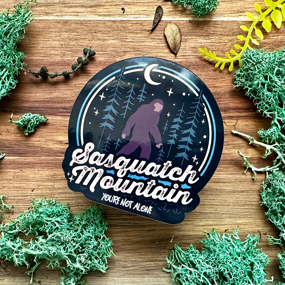 Sasquatch Mountain sticker on a wooden surface with foliage
