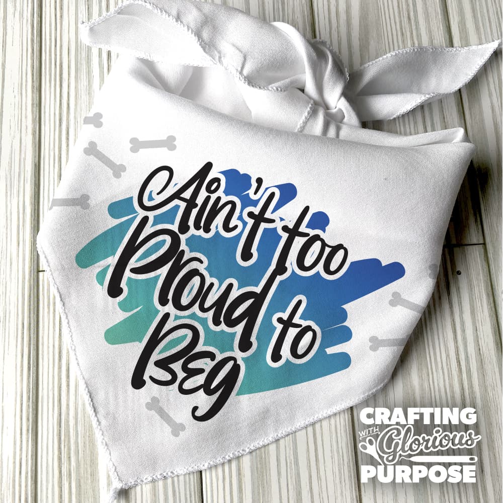 White bandana with blue paw print and text 'Ain't too Proud to Beg' on a wooden surface, with 'Crafting with Glorious Purpose' branding.